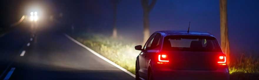 Auto bei Nacht auf einer Landstraße mit eingeschalteten Scheinwerfern und roten Rücklichtern